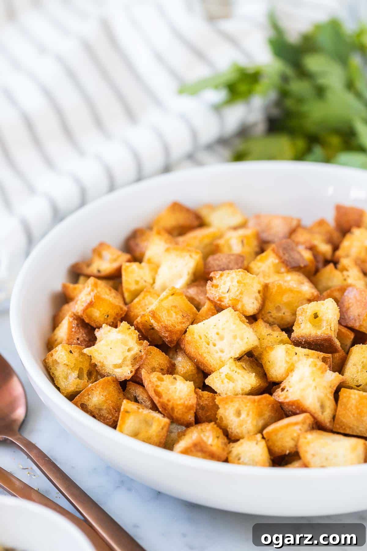 Crispy Air Fryer Croutons 6 A beautiful white bowl filled with air fryer croutons, accompanied by two elegant spoons, all set on a light background.