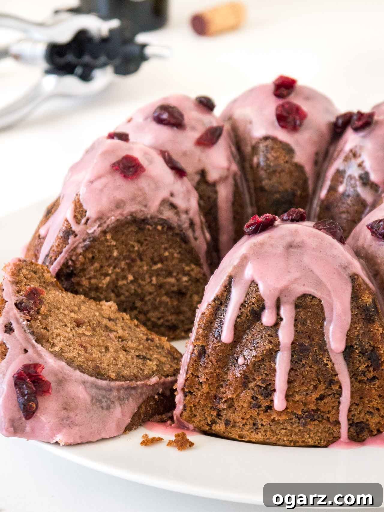 Chocolate Cranberry Bliss 4 A chocolate cranberry bundt cake with pink frosting, garnished with dried cranberries on a white plate. A piece of the cake has been cut out and is lying in front.