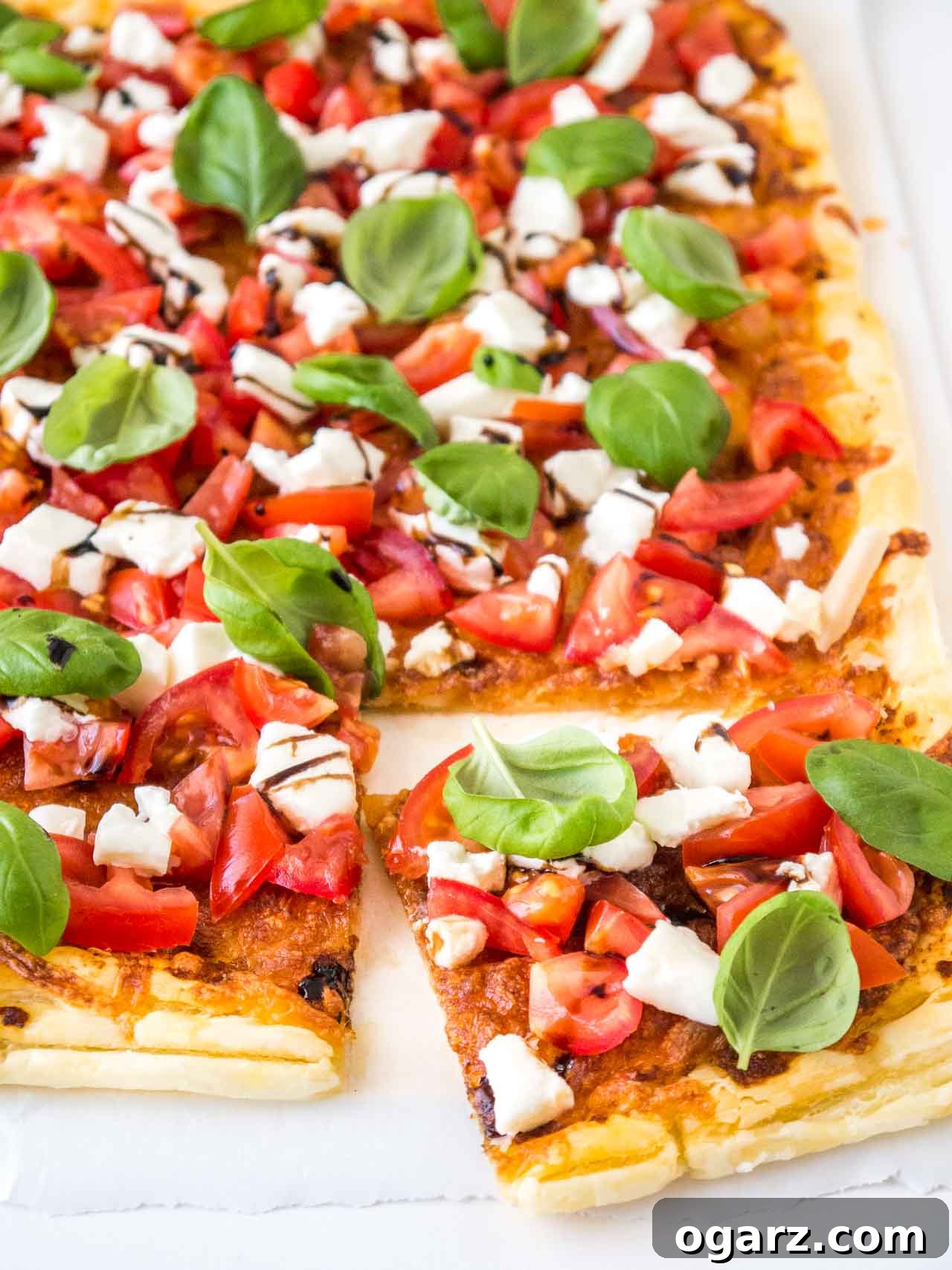 Puff Pastry Pizza with Fresh Tomato and Mozzarella 3 A perfectly baked Tomato Mozzarella Puff Pastry Pizza on a baking sheet, with a slice already cut, showcasing its flaky crust and fresh toppings.