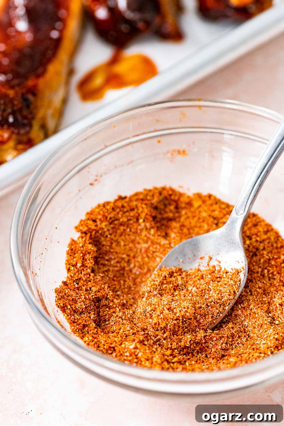 Ultimate Barbecue Blend 2 A glass bowl filled with BBQ seasoning and a spoon in it.