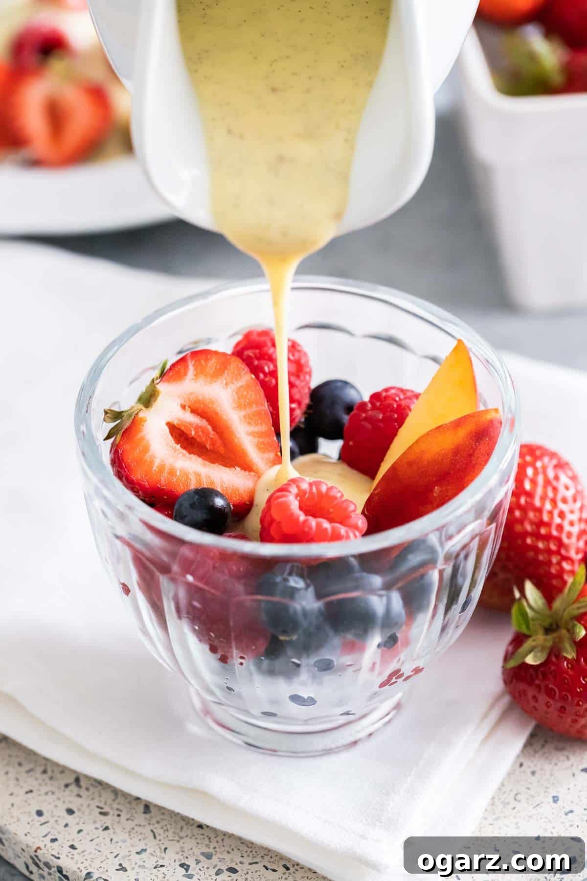 Silken Vanilla Crème 6 Velvety vanilla sauce being elegantly poured over a vibrant medley of fresh berries nestled in a glass bowl, showcasing its smooth texture.