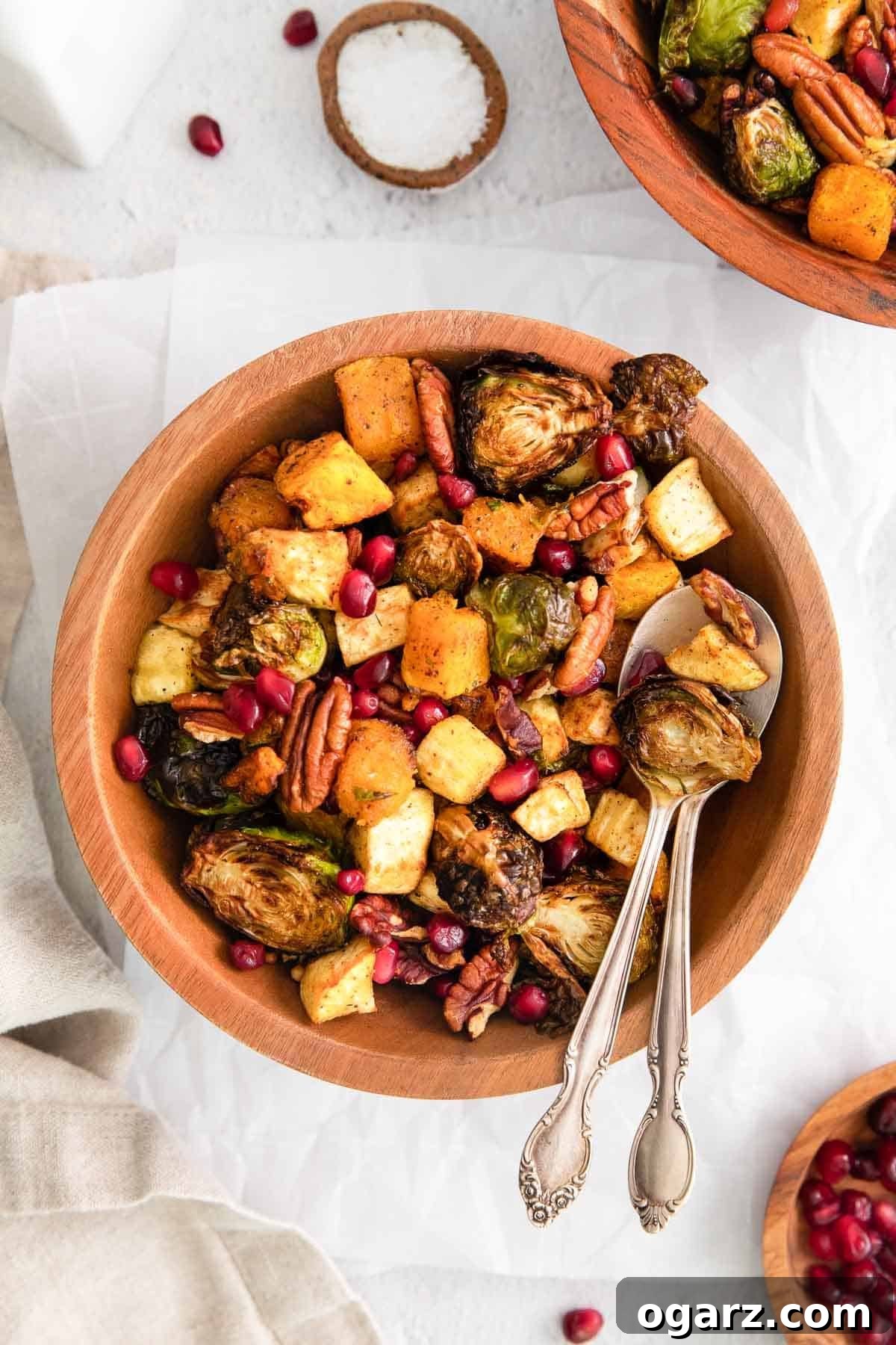 Golden Crispy Air Fryer Vegetables 2 A wooden bowl filled with beautifully roasted butternut squash, Brussels sprouts, parsnips, pecans, and pomegranate seeds, with a serving spoon tucked inside.