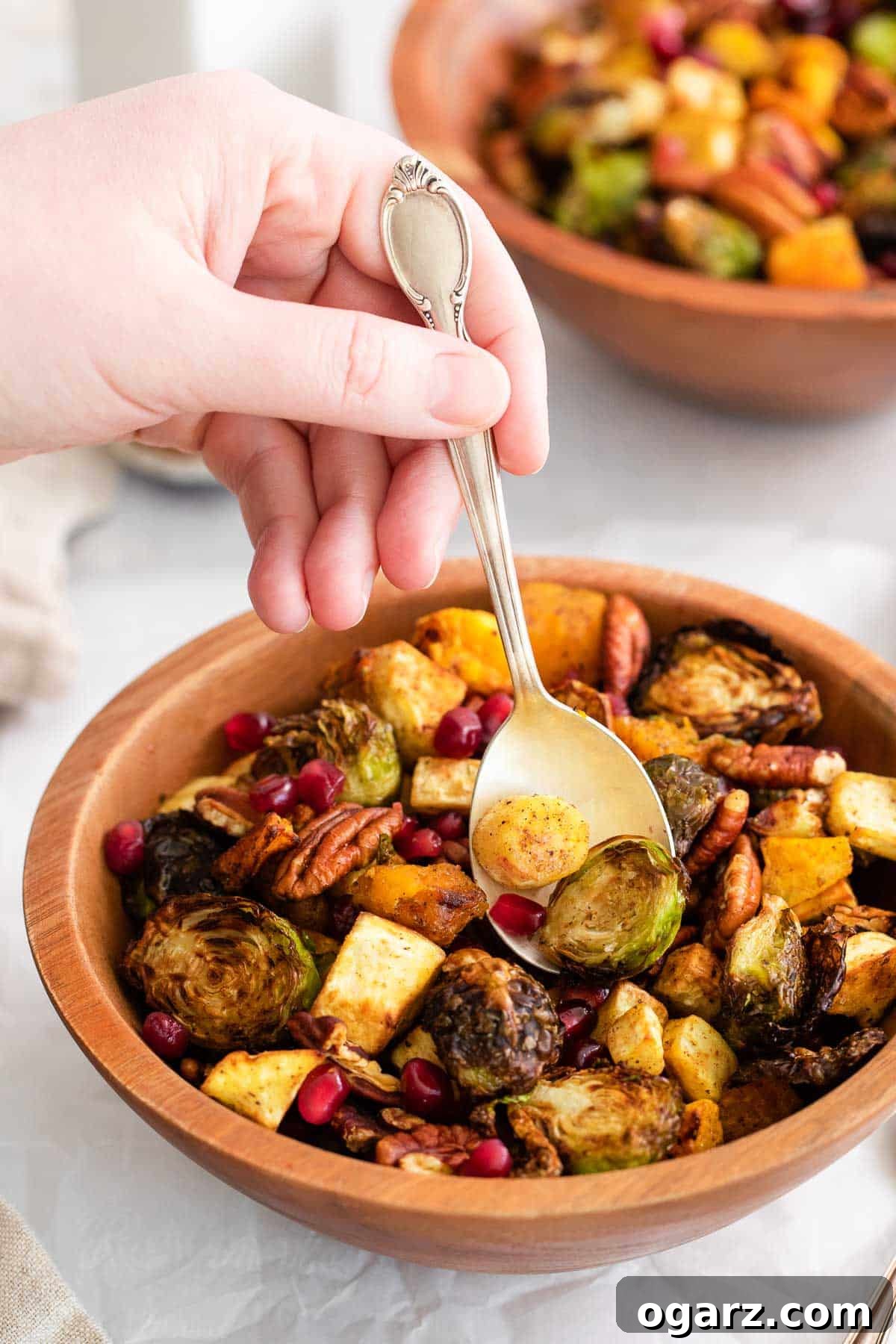 Golden Crispy Air Fryer Vegetables 5 A hand reaching into a wooden bowl with a serving spoon to scoop out air fryer roasted vegetables.