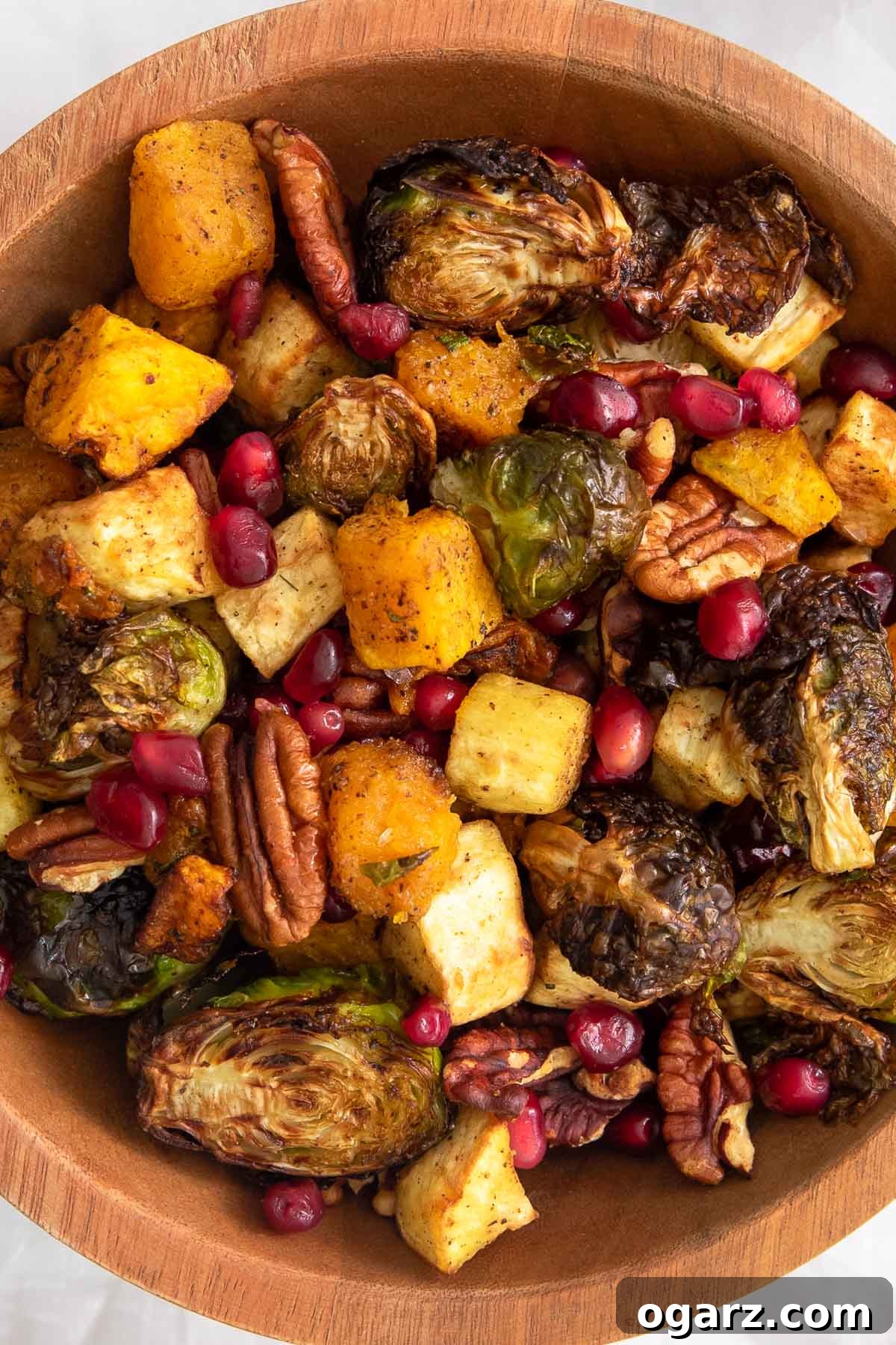 Golden Crispy Air Fryer Vegetables 6 A close-up of a wooden bowl filled with roasted butternut squash, Brussels sprouts, parsnips, and pecans, garnished with fresh pomegranate seeds.