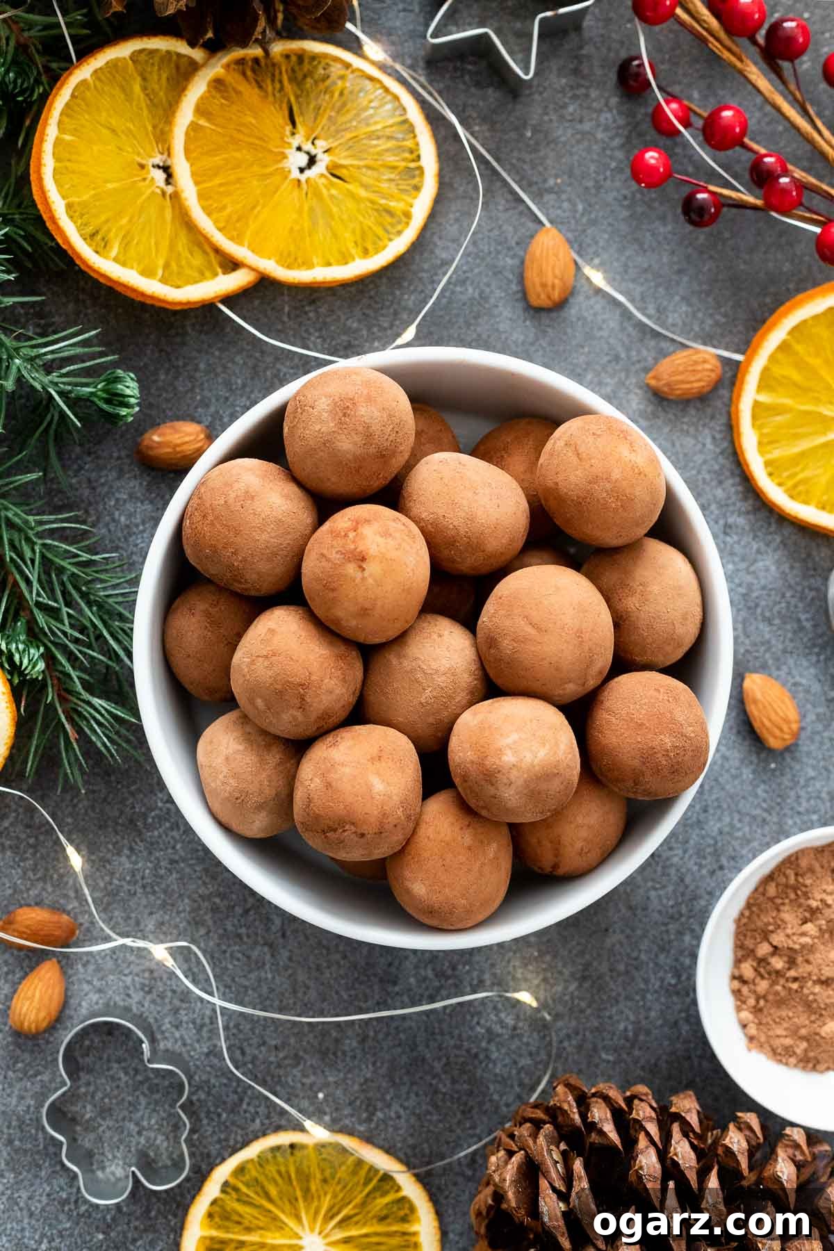 Marzipan Potato Treats 5 Marzipankartoffeln in a white bowl on a black board, next to it are orange slices and almonds, creating a festive display.