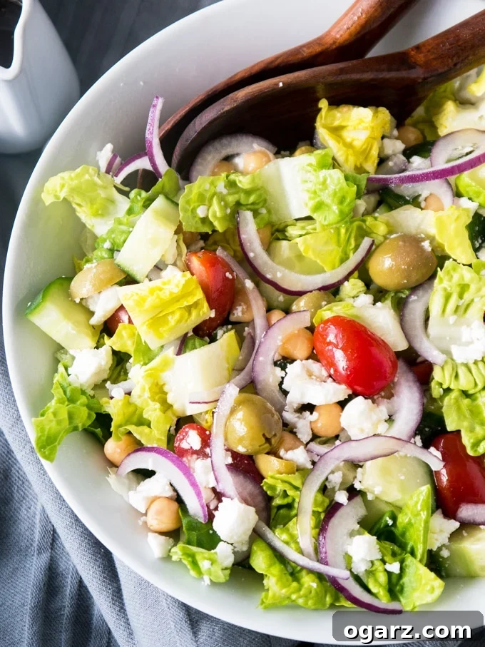 Refreshing Balsamic Chickpea Feta Greek Salad 3 Overhead view of a vibrant Balsamic Chickpea Feta Greek Salad, showcasing crisp shredded lettuce, halved bright grape tomatoes, briny green olives, thinly sliced red onion, diced cucumber, and generous crumbles of feta cheese and chickpeas, all mixed in a white bowl.