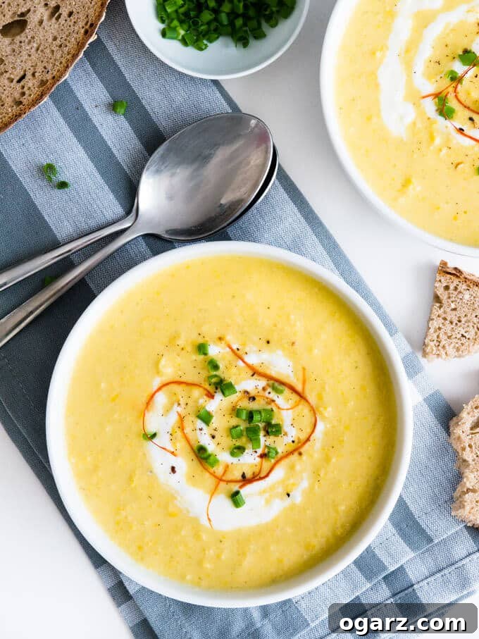 A close-up of the curried cream of corn soup, showing its smooth, vibrant yellow texture. A spoon is gently dipped into the bowl, ready to be enjoyed with a side of crispy bread.