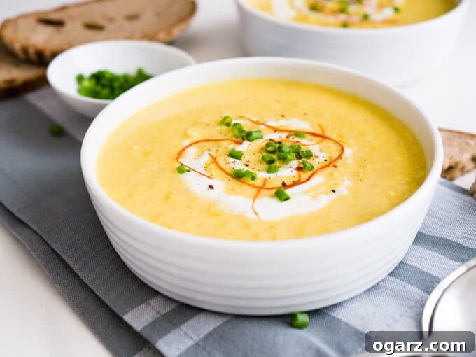 Three bowls of curried cream of corn soup, garnished with fresh herbs, on a wooden table. One bowl is in sharp focus, highlighting the creamy texture and inviting presentation.