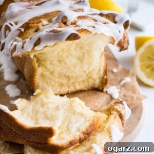 A lemon pull-apart bread with lemon glaze on a piece of brown parchment on a wooden cutting board next to some halved limes.