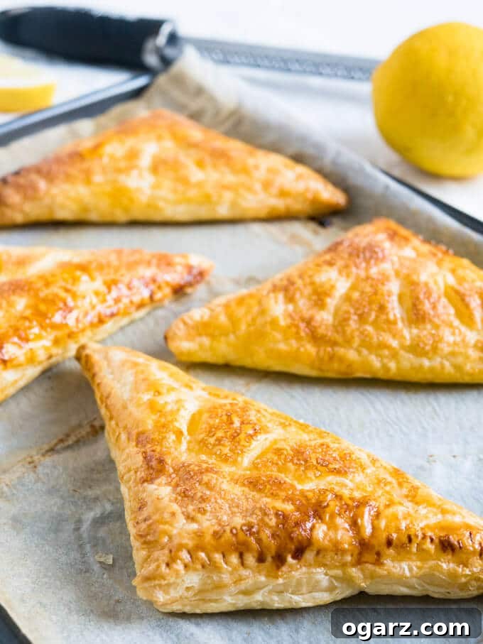 Zesty Lemon Puff Parcels 3 Close-up of baked Lemon Ricotta Puff Pastry Pockets on parchment paper, showing the crispy, sugar-caramelized crust.