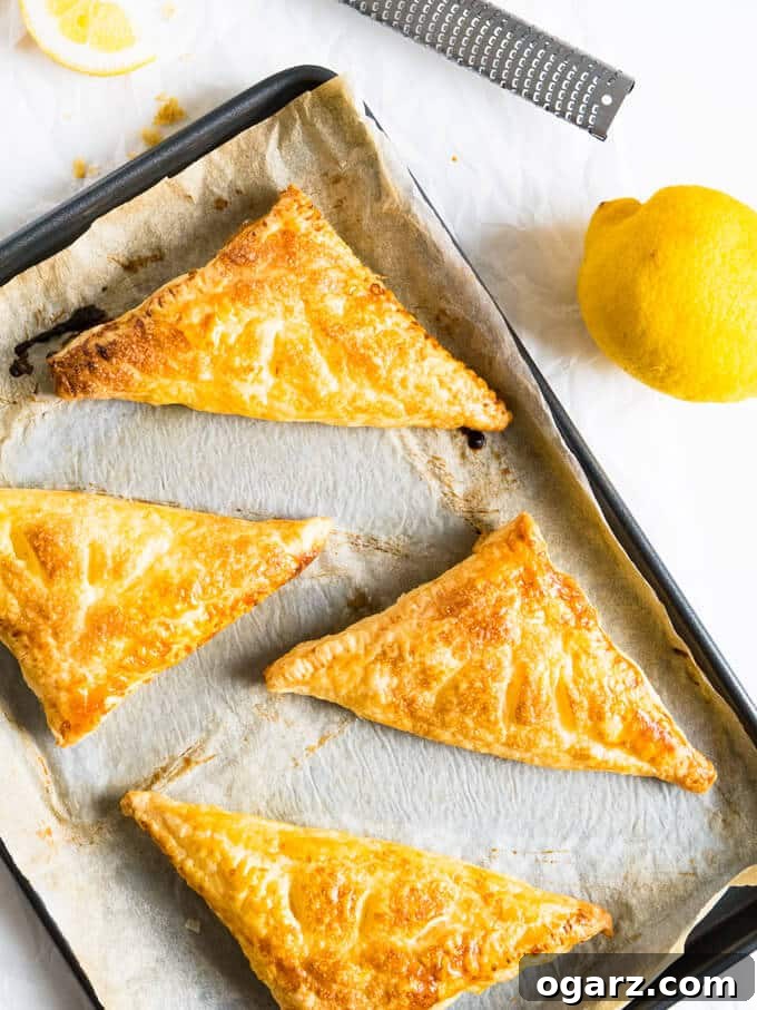 Zesty Lemon Puff Parcels 5 Close-up of two Lemon Puff Pastry Pockets, one bitten, showing the lemon ricotta filling, on a rustic wooden board.