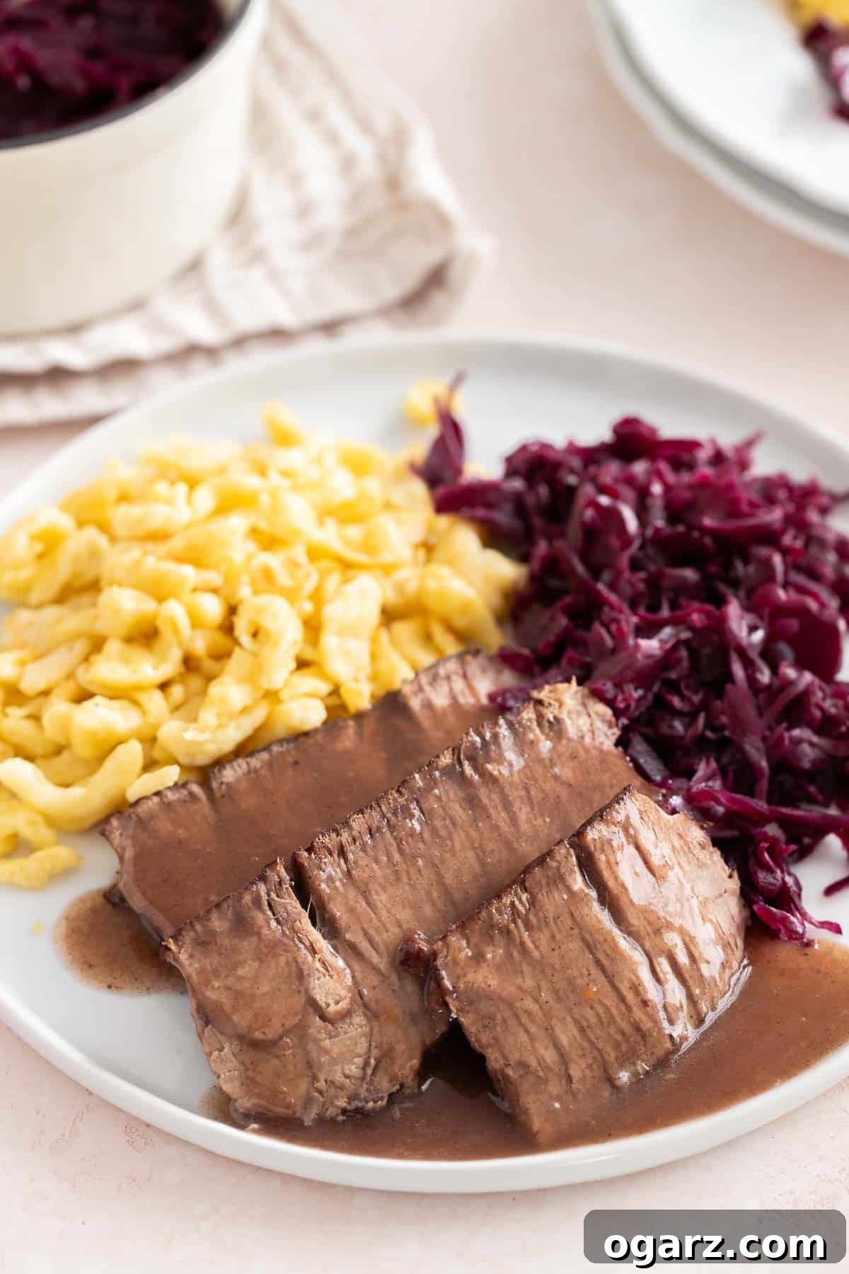Tangy German Pot Roast 2 Sauerbraten on a white plate with spaetzle and red cabbage.