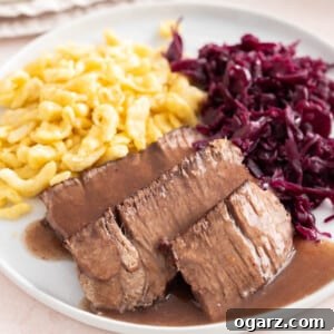 Tangy German Pot Roast 14 Sauerbraten on a white plate with spaetzle and red cabbage.