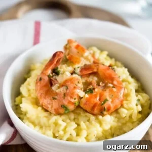 A white bowl with saffron risotto and fried shrimp on top on a wooden cutting board with a white dish towel with a red stripe.