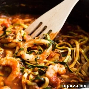 Ocean's Bounty Zucchini Marinara 5 A pan filled with Seafood Zucchini Marinara, featuring calamari and prawns in a rich tomato sauce, with a slotted spatula.