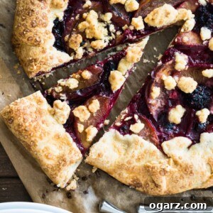 Top-down shot of a crostata with peaches and berries with a slice cut out, but left in place, on a wooden cutting board.