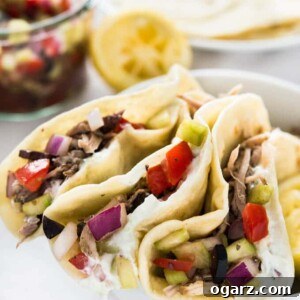 A white bowl with 3 greek style tacos, with pulled pork, greek salad and tzatziki. There's a jar of the greek salad, half a lemon and a plate of tortillas in the background.