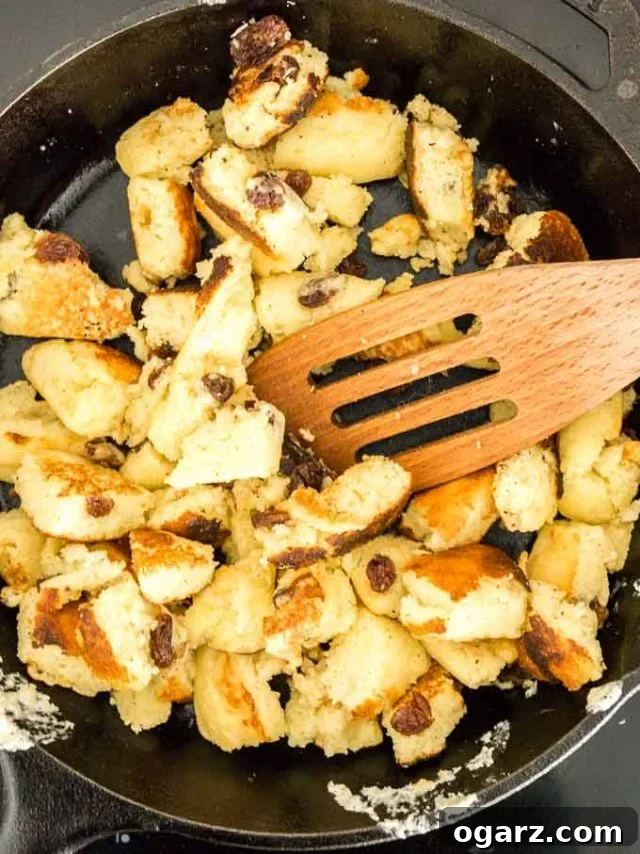 Kaiserschmarrn (Scrambled Pancakes) is an Austrian dessert that's also very popular in Bavaria! A sweet fluffy pancake made with rum-soaked raisins is torn into bite-sized pieces, caramelized, and served sprinkled with powdered sugar, applesauce, and preserves. This easy dessert recipe also tastes great for brunch and is loved by kids and adults alike! #Pancakes #DessertRecipes #Kaiserschmarrn #GermanRecipes #ComfortFood Torn, cooked pancakes with raisins in a lodge pan with a slotted wooden cooking spatula.
