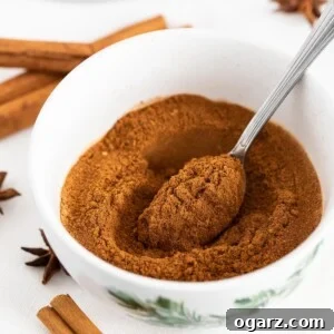 Yuletide Gingerbread Blend 7 A white bowl filled with ground spices and a spoon in it, next to cinnamon sticks and star anise