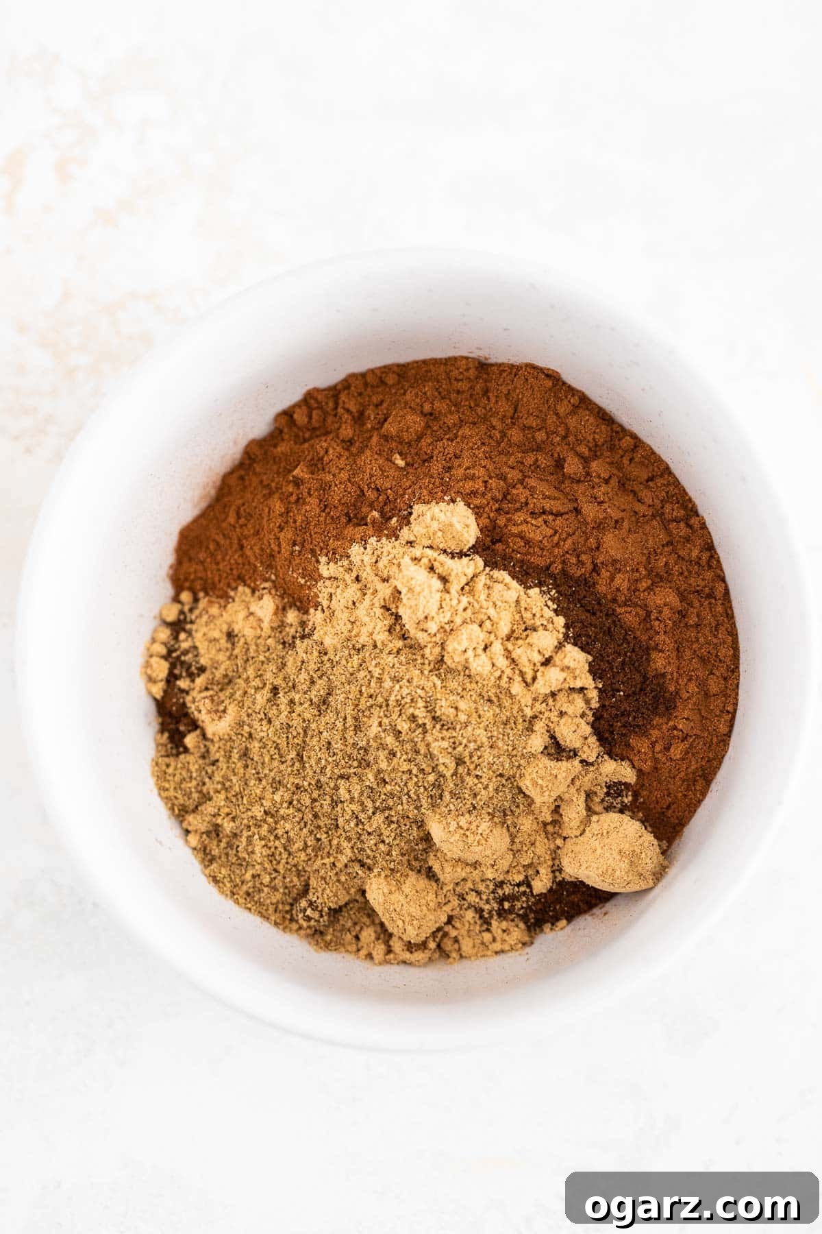 Yuletide Gingerbread Blend 4 Different ground spices in a white bowl on a white and beige background.