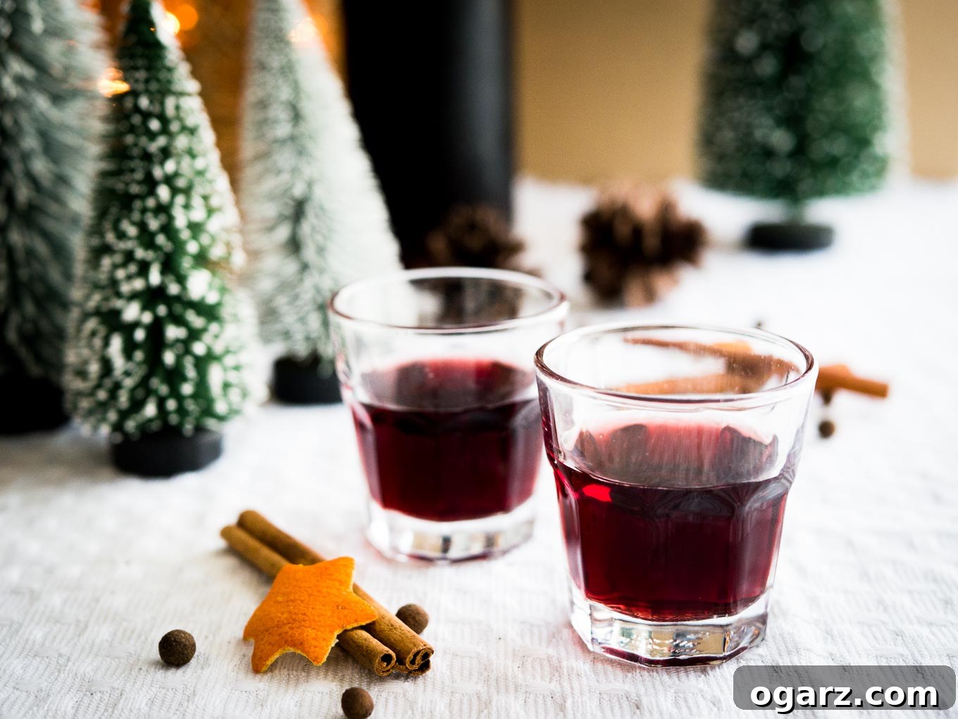 A festive table setting with two glasses of mulled wine liqueur, surrounded by winter decor like pinecones and greenery.