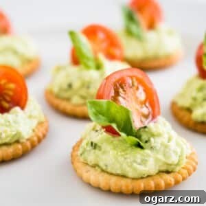 Mediterranean Tomato Feta Poppers 5 Feta tomato bites on white parchment paper. The bites consist of a cracker, with feta-basil spread topped with a tomato and basil.
