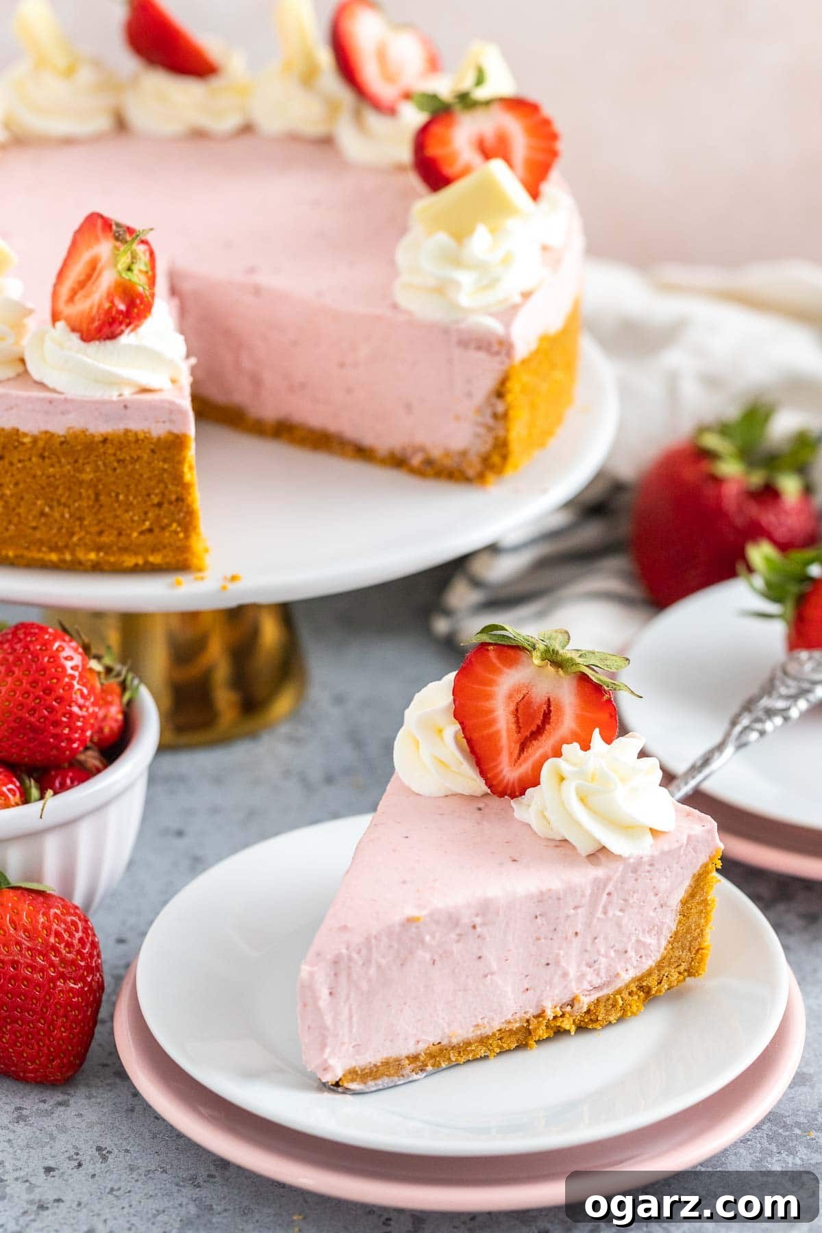 Effortless Strawberry Cheesecake Bliss 7 A perfect slice of no-bake strawberry cheesecake sitting next to the whole cake on a decorative plate.