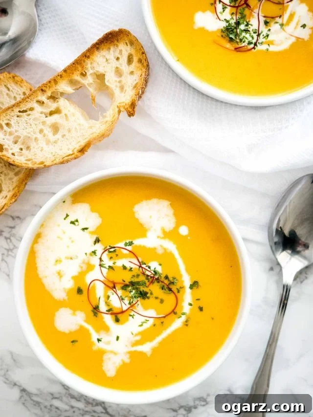 Creamy Instant Pot Carrot Soup 3 A top-down view showcasing two inviting bowls of Instant Pot Carrot Soup, each adorned with a dollop of sour cream and a sprinkle of vibrant chili threads. Two perfectly toasted slices of bread lie beside them on a crisp white tablecloth, suggesting a delightful and comforting meal.