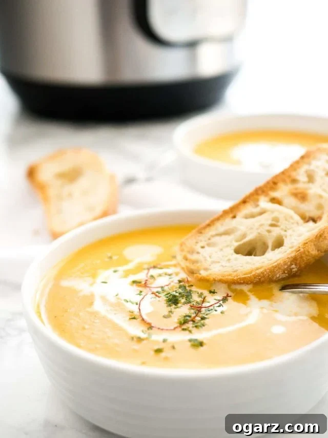 Creamy Instant Pot Carrot Soup 6 A beautifully presented bowl of creamy Instant Pot Carrot Soup, artfully garnished with a swirl of sour cream and delicate chili threads. It's served with a toasted slice of rustic bread and a spoon, with an Instant Pot and another bowl of soup subtly visible in the background, creating a comforting kitchen scene.