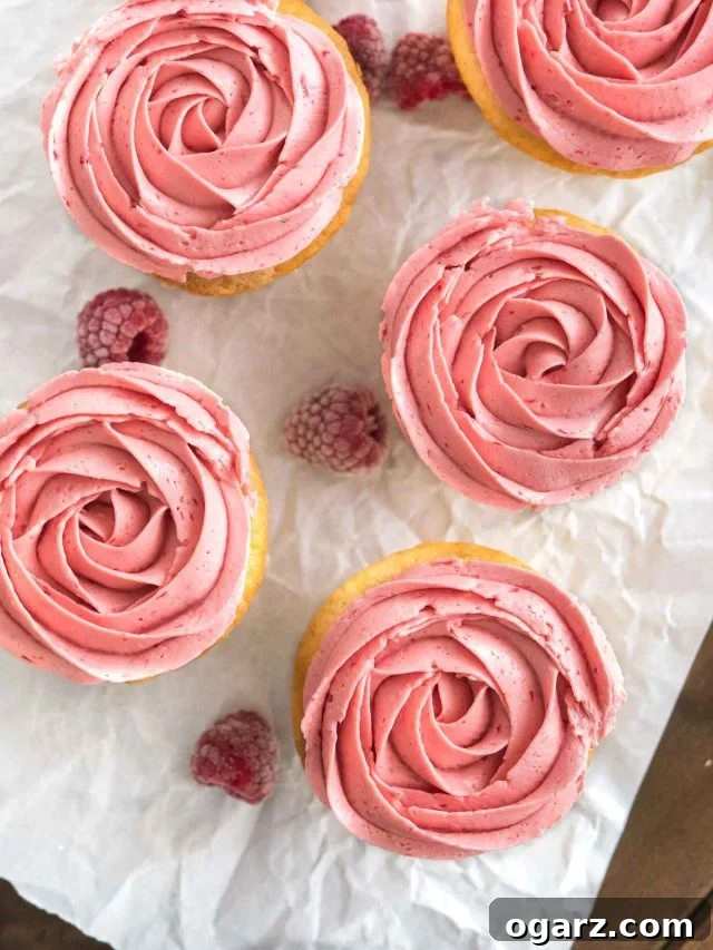 Top-down shot of raspberry lemon cupcakes with pink raspberry frosting next to some raspberries on parchment paper.