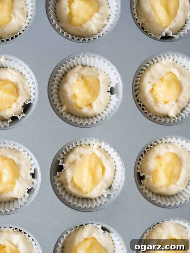 Top-down shot of a muffin pan, lined with muffin liners, filled with batter and dollops of lemon curd.