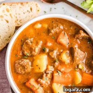 A bowl of beef stew with a spoon and bread next to it
