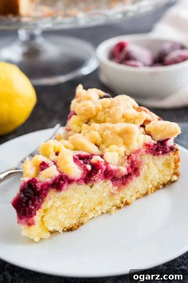 Effortless Lemon Raspberry Delight 2 A delectable slice of lemon raspberry cake with a golden streusel topping, served on a white plate with a fork, accompanied by a fresh lemon and vibrant raspberries in the background.