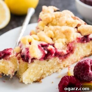 Effortless Lemon Raspberry Delight 5 A slice of lemon raspberry cake with streusel topping on a white plate with a fork with a small piece of the cake on it, garnished with lemon and raspberries.