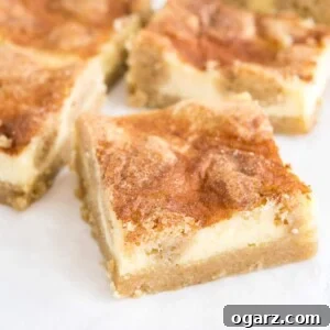 Cinnamon Sugar Snickerdoodle Cheesecake Bars 6 Some snickerdoodle cheesecake bars sitting on parchment paper. The frontmost is turned 45 degrees, ready to be enjoyed.