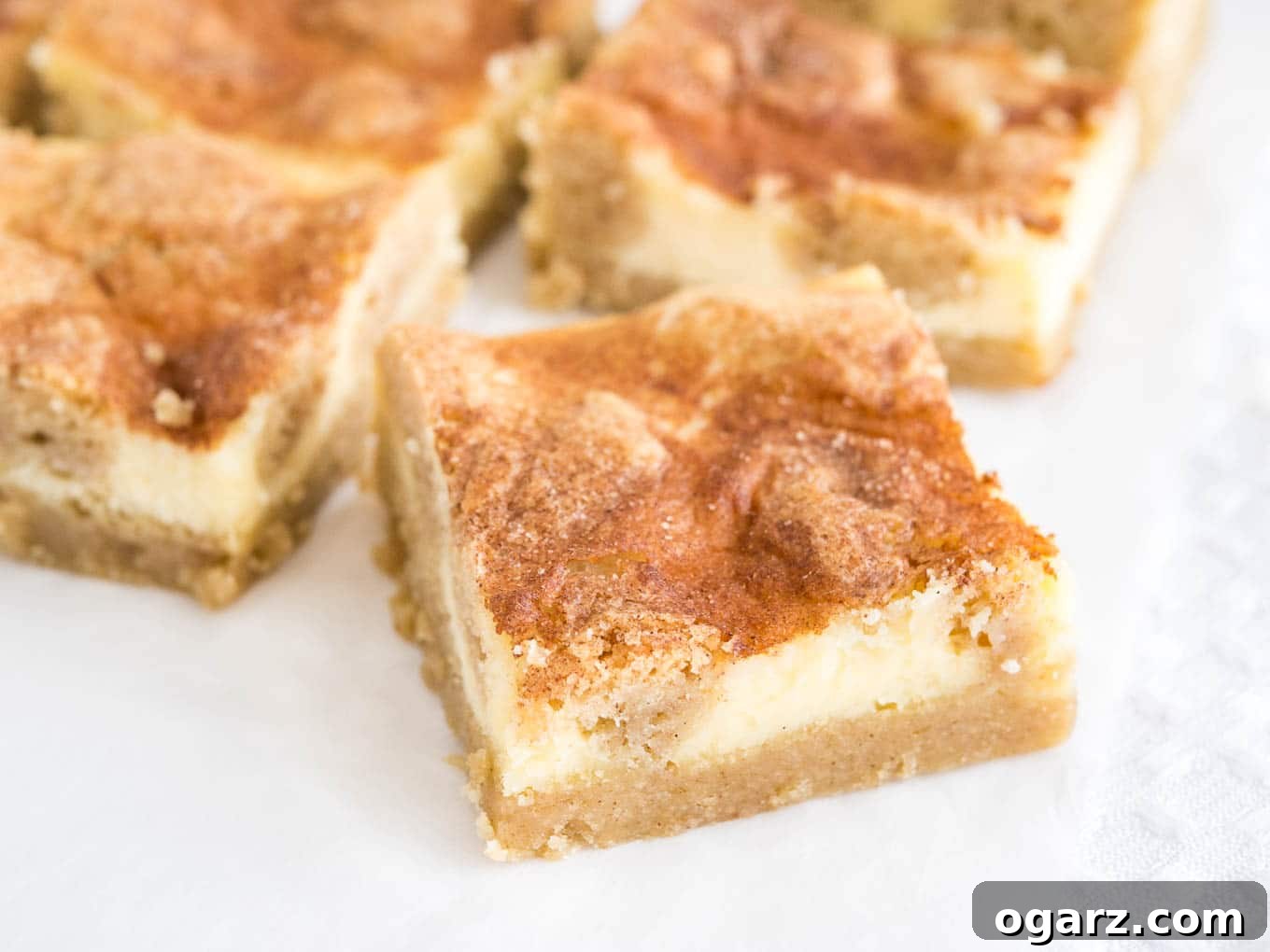 Cinnamon Sugar Snickerdoodle Cheesecake Bars 7 Some snickerdoodle cheesecake bars sitting on parchment paper, ready to be picked up and enjoyed.