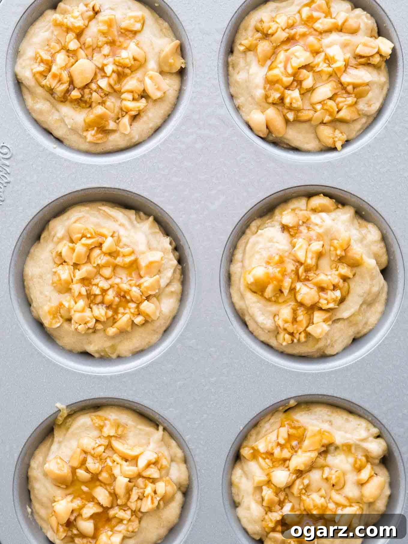 Peanut Butter Banana Bliss Muffins 4 Top-down shot of a grey muffin pan with muffin batter topped with peanuts before baking.