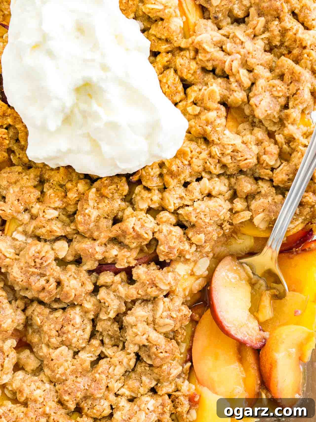 Top-down shot of a glass baking dish with a layer of peaches topped by a layer of crisp on a white dishtowel, garnished with whipped cream.