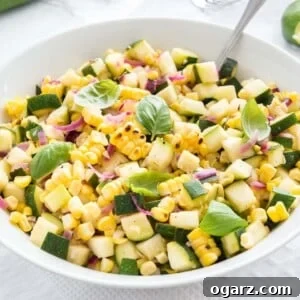 Roasted corn zucchini salad with onions in a white bowl, garnished with basil, with a spoon in it