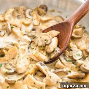 Mushroom Chicken Pasta sauce with cream in a stainless steel pan, with a wooden cooking spoon in it.