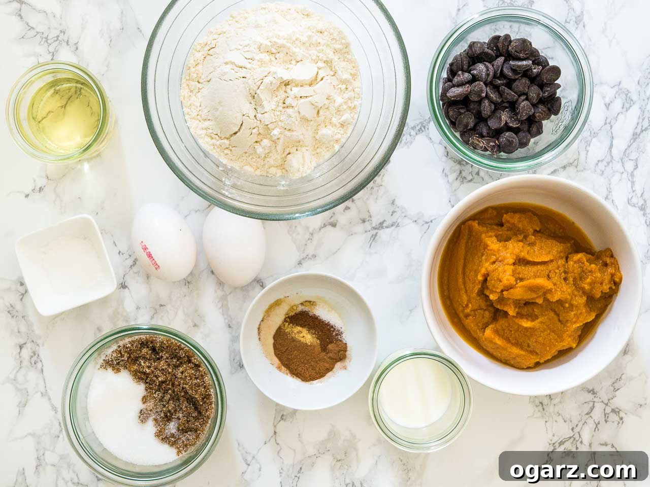 Harvest Spice Pumpkin Chocolate Chip Muffins 3 Top-down shot of ingredients in assorted bowls: flour, brown sugar, white sugar, oil, vanilla extract, eggs, pumpkin puree, mil, baking powder, baking soda, cloves, cinnamon, ginger, nutmeg, allspice, salt.