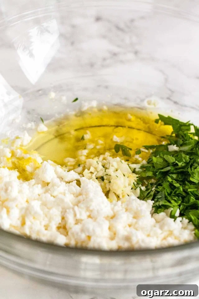 A vibrant assortment of fresh ingredients for Greek-Style Boiled Potatoes displayed in glass bowls on a elegant marble surface, including golden olive oil, minced garlic, bright lemon juice, crumbled feta, and fresh chopped parsley.