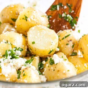 A glass bowl of Greek-Style Boiled Potatoes with feta and parsley, served with a wooden spatula.