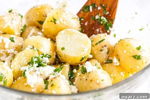 A glass bowl showcasing the freshly prepared Greek-Style Boiled Potatoes, garnished with vibrant feta and fresh parsley, served with a wooden spatula.