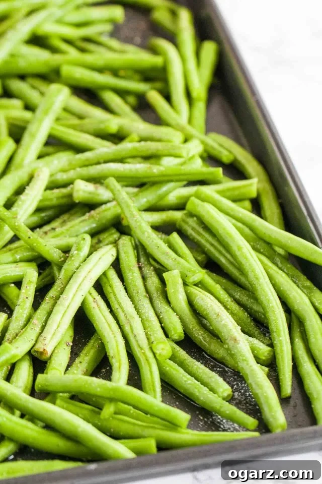 Uncooked green beans on a baking sheet with salt and pepper, prepared for oven roasting.