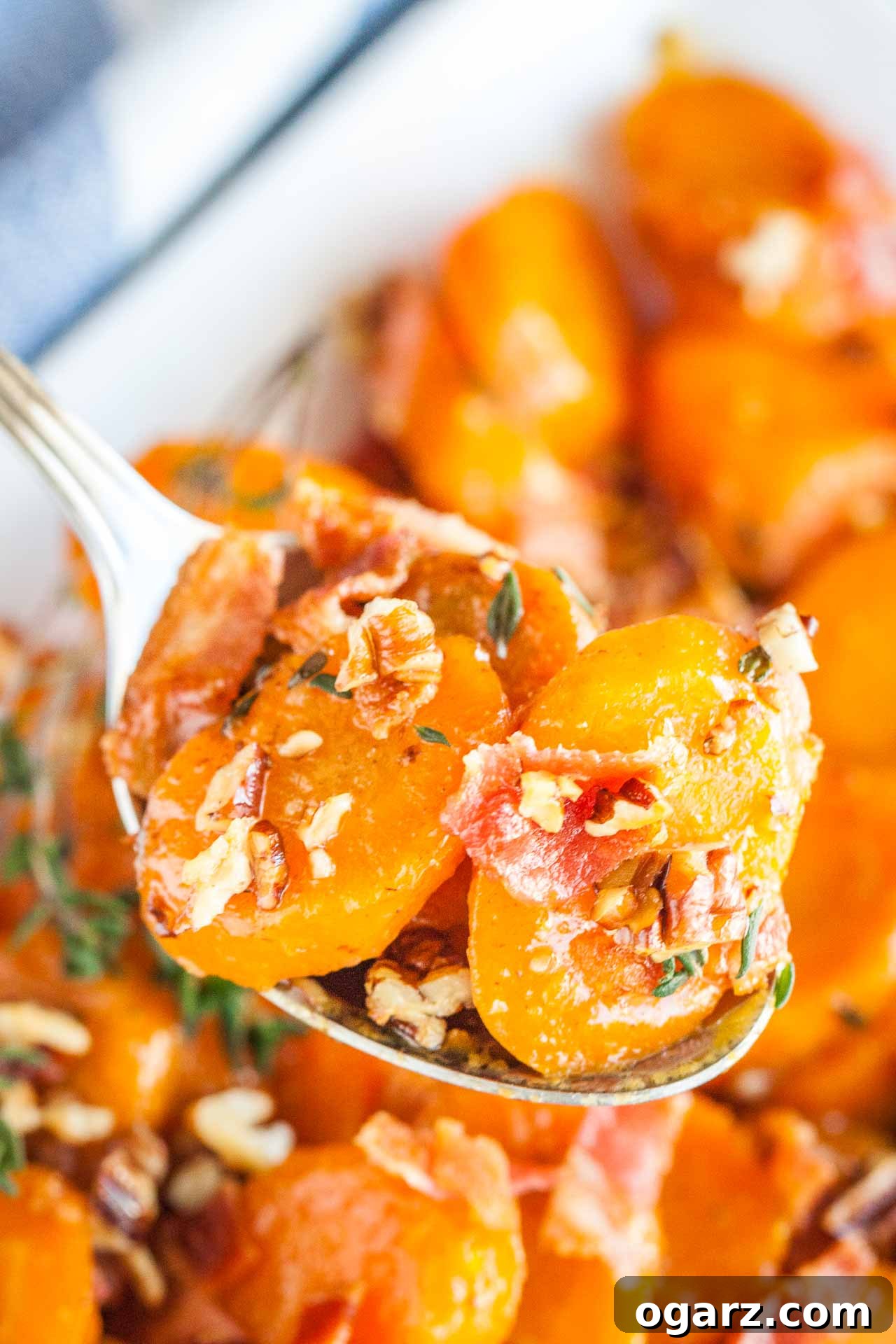 Brown Sugar Carrots: A Sweet Side Dish 3 A spoon holding up some brown sugar-glazed carrots with bacon and pecans above a white bowl of carrots.