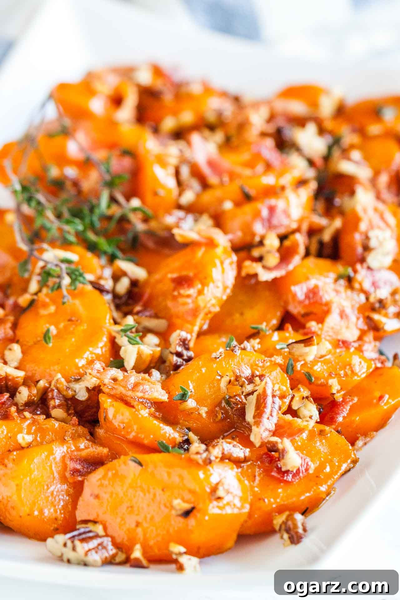 Brown Sugar Carrots: A Sweet Side Dish 4 Close-up of a rectangular white plate of brown sugar-glazed carrots with bacon and pecans garnished with thyme.