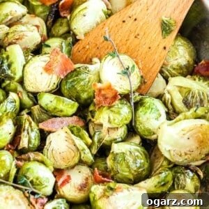 Crispy Brussels Sprouts with Smoked Pork Belly 6 Roasted brussels sprouts with bacon and a sprig of thyme with a wooden cooking spatula in it in a stainless steel pan.