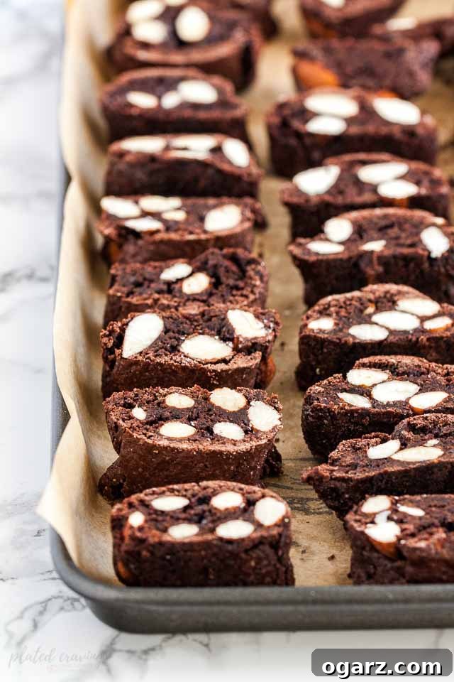Slices of biscotti lying on a baking sheet lined with parchment paper on a marble surface.
