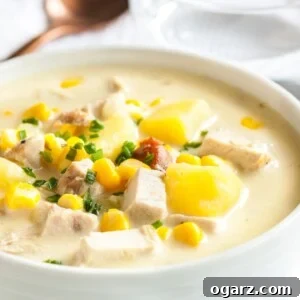 A white bowl of creamy leftover turkey soup, garnished with chives on a white dishtowel with a bronze spoon next to it.